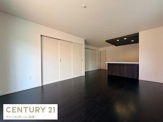 リビングには開放感のあるスペースが広がっています。ダークカラーのフローリングが空間に落ち着きを与えています。白い壁と天井が室内を明るく演出します。キッチンとの一体感も魅力のひとつです。