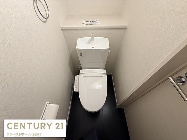 シンプルなデザインのトイレです。ホワイトとダークカラーの床が調和し清潔感のある印象です。使い勝手を考えた配置になっています。収納棚も備わっています。ペーパーホルダーやタオルリングが設置されています。