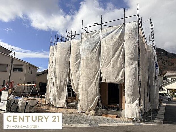 建築中の住宅現場の様子が確認できます。足場や覆いシートもしっかりと設置されています。周囲には住宅が立ち並び街並みも感じられます。進捗状況が分かりやすい外観写真です。