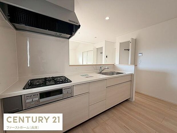 明るい色合いのキッチンで清潔感があります。収納スペースも充実しており使いやすい構造です。ガスコンロや換気扇も設置されています。リビングと一体感のある設計です。