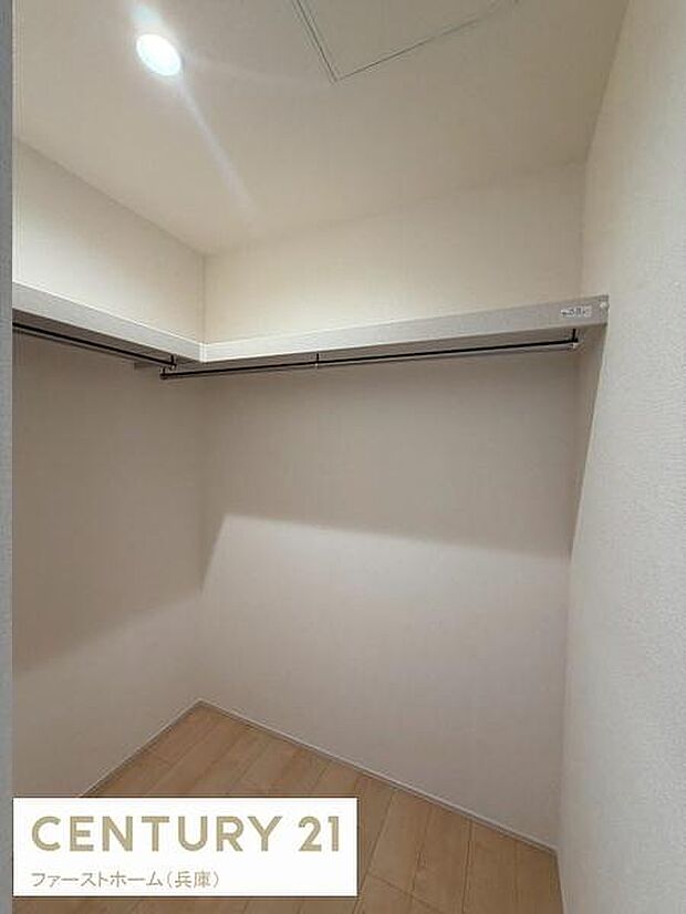 明るい照明が印象的な収納スペースです。ハンガーパイプが両側に設置されているため使い勝手が良好です。天井も高めで空間を有効に活用できます。床は木目調で清潔感があります。収納内部もシンプルなデザインです。