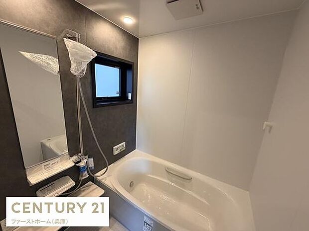 シンプルなデザインで清潔感があります。窓付きで換気しやすいバス空間です。ミラーや棚も設置されており使いやすさを重視しています。ダークトーンの壁面が特徴的です。設備の配置も無駄がなくすっきりしています。