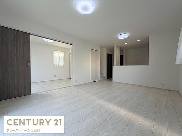 明るい色合いの床材が広がりを感じさせるリビングです。複数の照明で室内がしっかりと照らされます。開放感のある空間が特徴です。窓から自然光も取り入れやすい設計です。