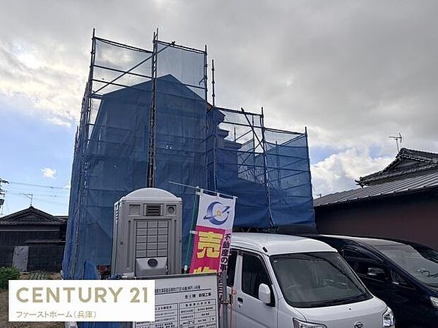 新築工事中の物件です。青い足場ネットが設置されており現場の安全にも配慮されています。仮設トイレも設置されているため作業環境が整っています。敷地内に車を駐車できるスペースも確認できます。