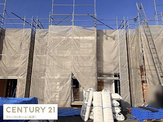 建築中の現場写真です。外壁部分には足場と防塵ネットがしっかりと設置されています。資材も整然と搬入されており作業が着実に進行している様子が見受けられます。現場のクリーンな状態が印象的です。