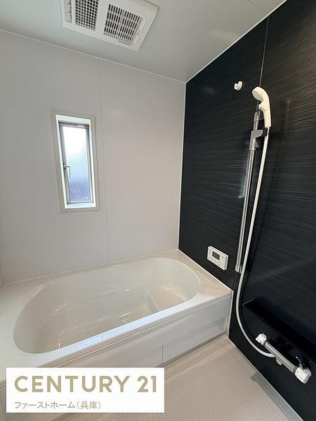 窓付きで換気しやすいバスルームです。壁の一面がダークカラーで空間に落ち着いた印象を与えています。浴槽はゆったりとしたサイズ感です。天井には換気設備も備わっています。シャワー付きで利便性も感じられます。