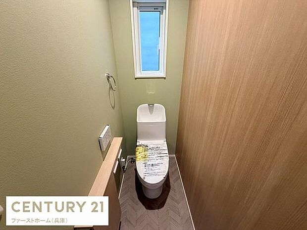 窓が設けられており換気しやすいトイレです。シンプルな内装が落ち着いた印象を与えます。機能的なデザインで使いやすさが考慮されています。木目調の壁が温かみをプラスしています。手洗い器付きで便利です。