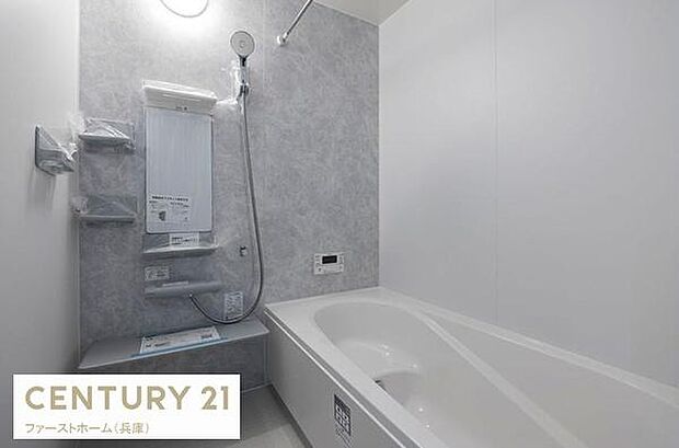 シンプルで清潔感のあるバスルームです。壁面のグレーのパネルが落ち着いた雰囲気を演出しています。浴槽はスペースにゆとりがありリラックスできる空間です。収納棚も付いており使い勝手に配慮されています。