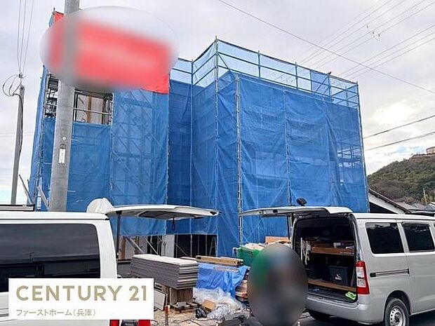 建築中の現場の様子が確認できる物件です。外壁部分には足場とブルーシートが設置されています。敷地内には複数台の車両も駐車できるスペースが見受けられます。周辺環境も開放的な印象です。