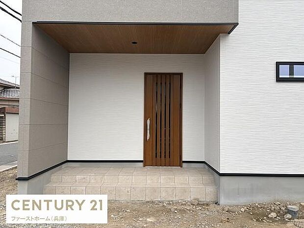 玄関はシンプルで洗練されたデザインが印象的です。木目調のドアが温かみを感じさせ外壁との調和も良好です。屋根付きのスペースが突然の雨にも対応しやすい仕様です。段差も低めで使いやすさを考慮されています。