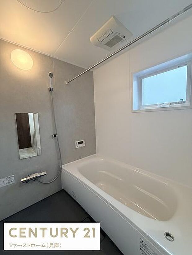 白とグレーを基調とした落ち着いたデザインのバスルームです。室内が明るく清潔感があります。浴槽が広めでゆったりとした印象です。窓があり換気や採光にも配慮されています。機能的なシャワー設備も備えています。