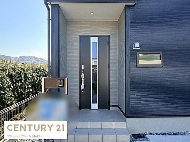 スタイリッシュな玄関ドアが印象的です。シンプルでまとまりのある外観が特徴です。玄関周りがゆったりしていて使いやすい設計です。機能的なポストが設置されています。外壁の質感が現代的です。