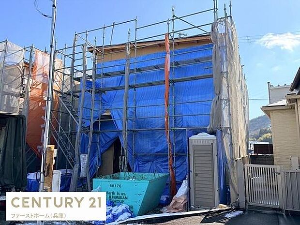 建築中の現場写真です。周囲は住宅街で落ち着いた雰囲気が感じられます。足場がしっかり設置されており工事が順調に進んでいる様子です。資材置き場や仮設トイレも整備されています。