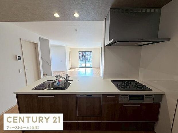 広々としたワークトップが印象的なキッチンです。3口コンロと換気設備も整い機能的な空間となっています。ダークブラウンのキャビネットが室内に落ち着いた雰囲気を与えます。