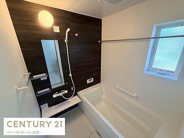 バスルームは明るい照明とダークブラウンの壁面が特徴でモダンな雰囲気が感じられます。使い勝手の良い大きめの浴槽と便利な手すりが設置されています。窓があるため自然光が入りやすく換気にも配慮された設計です。