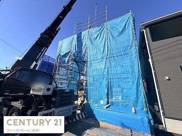 新築物件の建築現場です。クレーンを使った工事が進行しており現場は整理整頓されています。青空の下で建築作業が行われています。周辺には他の建物も確認できます。家づくりの基礎からしっかりと進んでいます。