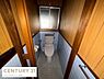 トイレ：木目調の壁面とブルーのタイルが落ち着いた印象を与えるトイレです。窓があるため日中は自然光が差し込みます。ペーパーホルダーやタオル掛けも備わっています。独立した空間でプライバシーも確保されています。