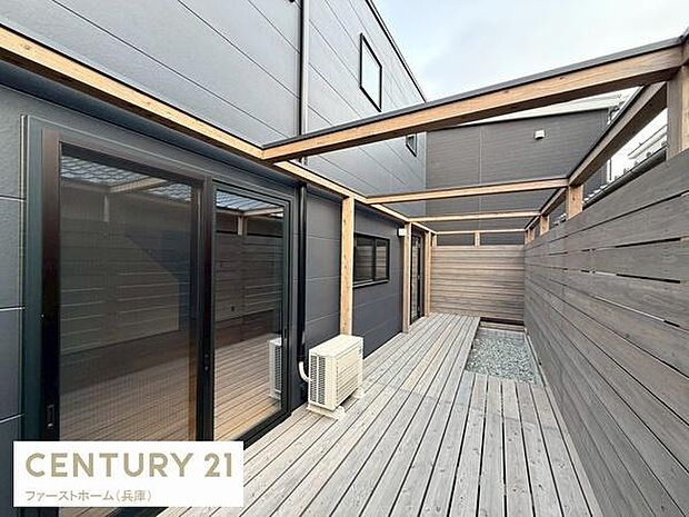 木目調の外観とウッドデッキが印象的な空間です。屋根付きスペースが採光と開放感を演出しています。室外機も設置されており快適にご利用いただけます。目隠しフェンスがプライバシーに配慮されています。