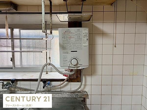 シンプルなタイル壁が特徴のキッチンスペースです。窓からの採光が期待できる造りとなっています。給湯器が設置されており日常生活に便利です。配管や水栓部分も確認しやすい位置に配置されています。