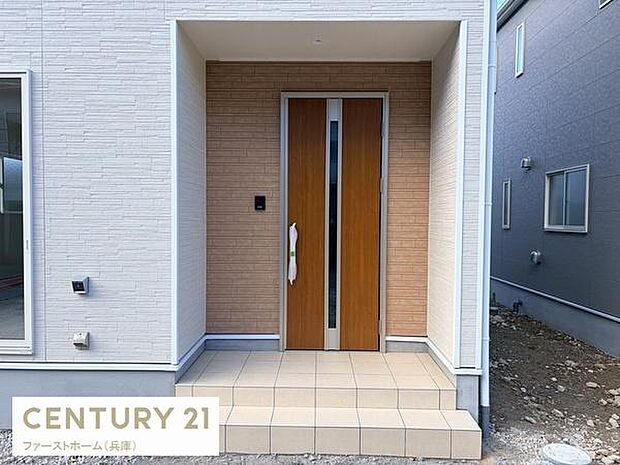 シンプルでモダンなデザインの玄関です。広めのタイルスペースが印象的です。木目調の扉がアクセントとなっています。周囲の外壁とのバランスも良好です。落ち着いた色合いの玄関となっています。