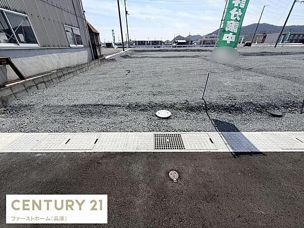 広々とした現地土地写真です。道路に面しており整った区画が印象的です。周辺には建物が少なく開放感があります。敷地内の設備も確認しやすい配置となっています。現地の様子がしっかりと分かる写真です。