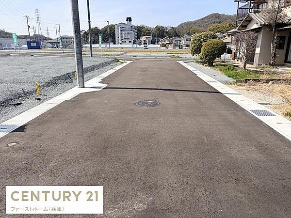 前面道路は舗装が整っており周辺環境も見通しが良い印象です。周囲に建物が点在し区画整備もきちんとされています。電柱やマンホールなどインフラ設備も整っています。土地利用計画にも適した現地写真です。