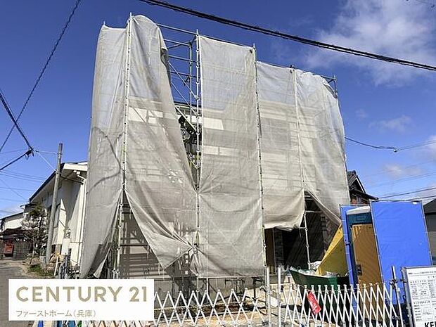 建築中の住宅の外観が写っています。足場やシートによる安全対策が施されており現場管理が整っています。周囲の住宅街との調和も感じられます。晴天の下での撮影により明るい雰囲気が伝わります。