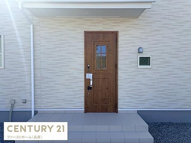 玄関ドアの木目調デザインが印象的です。広々としたポーチで余裕のある空間が確保されています。シンプルな外壁が清潔感を演出しています。屋根付きで雨天の出入りも安心です。