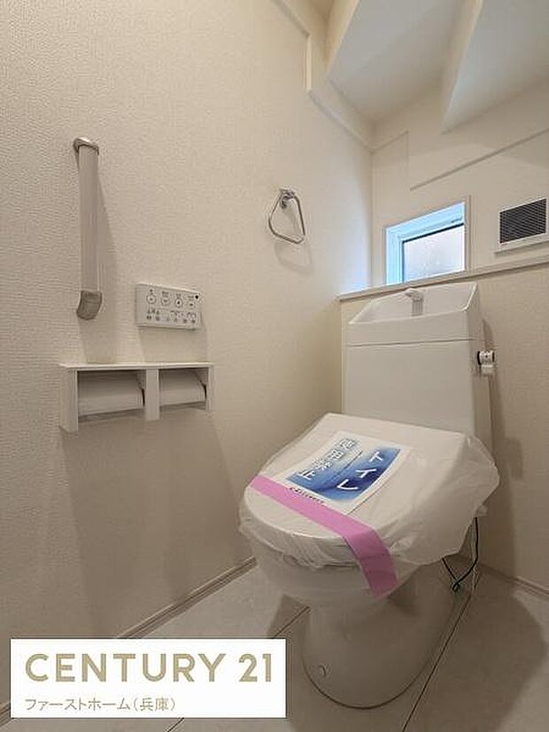 トイレ内はシンプルですっきりとしたデザインです。壁に設置された操作パネルが特徴的です。窓があり明るい空間です。手すりも備え付けられています。清潔感を感じられるトイレです。