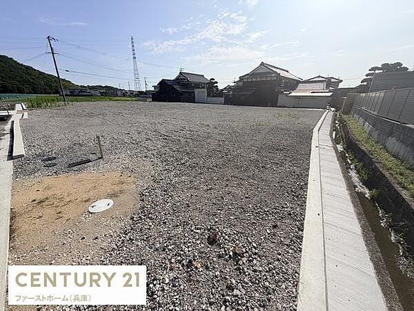 現地土地写真が示すように広々としたスペースが確保されています。周辺に既存の住宅もあり環境の様子がわかります。道路や側溝も整備されており生活の基盤がしっかりしています。陽当たりも確認できる写真です。