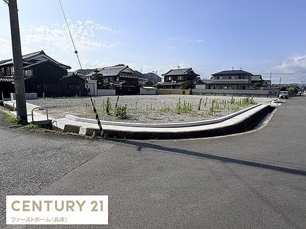 角地に位置する現地土地写真です。周囲は落ち着いた住宅が並びゆったりとした区画が広がっています。前面道路も広く開放感のある立地が特徴です。日当たりも良好で建築にも適しています。