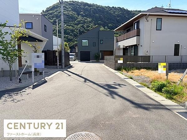 周囲に住宅が並ぶ穏やかな現地からの眺望です。道幅も広く開放感のある印象です。日当たりが良く前方には緑豊かな山も望めます。周辺環境もきれいに整備されています。