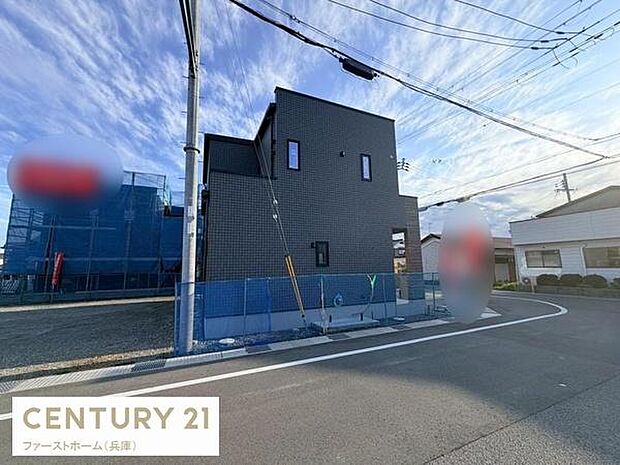 角地に位置する現地写真です。道路幅員が広く車の出入りもしやすい環境が確認できます。周囲は開放感があり建物の外観もシンプルで印象的です。前面道路も整備されており清潔感が感じられます。