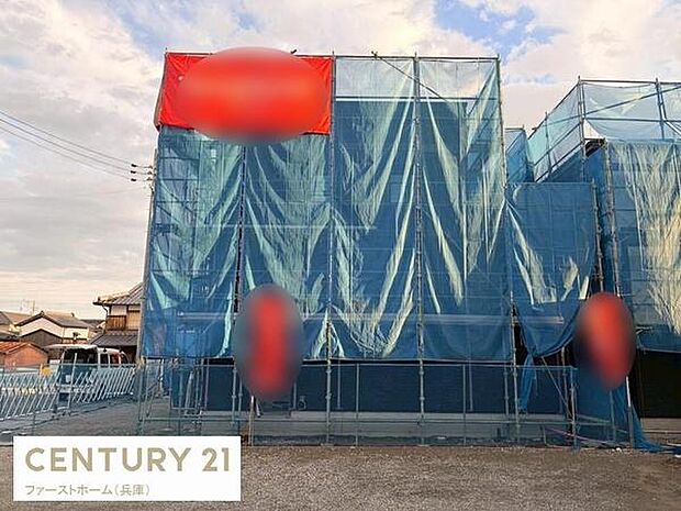 建物の外観はブルーのシートで覆われており工事の進行が分かりやすい状態です。周囲には住宅が立ち並び整然とした街並みが感じられます。空模様も穏やかで現場の様子がしっかり確認できます。