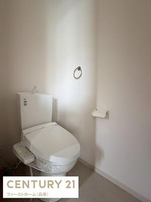 シンプルで清潔感のあるトイレ空間です。壁が広く圧迫感がありません。ペーパーホルダーやタオルリングも設置されています。床材も落ち着いた色合いでまとまっています。