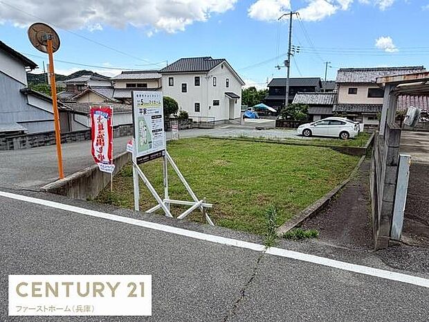 道路に面した現地土地写真です。周囲には住宅が並び整った区画が特徴的です。車の進入もスムーズに行えそうです。近隣環境の様子も確認できます。表示看板も設置され現地の状況が一目で分かります。