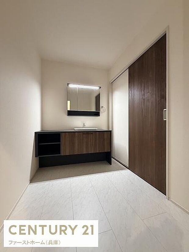 洗面台と洗面所がシンプルなデザインでまとめられています。落ち着いた色合いの木目調がアクセントになっています。広々とした空間が確保されており使い勝手の良さが感じられます。収納スペースも充実しています。