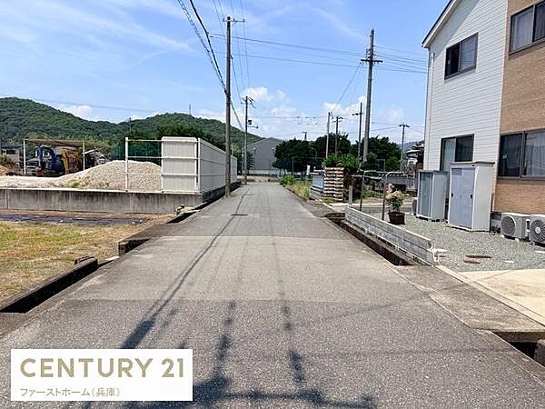 現地前面道路は舗装されており周囲には住宅や工事現場が見られます。道幅も確保されているため車の通行も安心です。電線や街灯も整備されていて暮らしやすさに配慮されています。