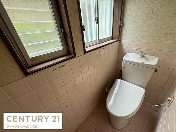 窓が2つあり換気がしやすいトイレです。タンク上の手洗い場付きで使い勝手も良好です。ナチュラルなタイルと壁紙が落ち着いた印象を与えます。明るさを感じられる空間です。