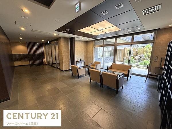 広々としたエントランスは窓からの自然光が心地よく差し込み開放感が感じられます。上質なソファとテーブルが配されゆったりとした空間が広がります。室内は落ち着いた色合いでまとめられており印象的な雰囲気です。