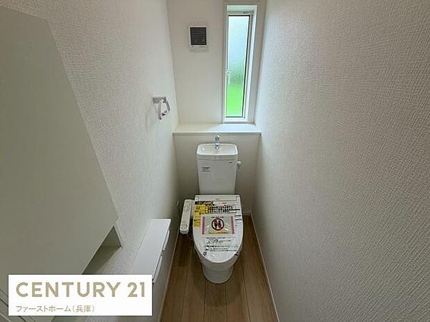 小窓付きで通気性を確保しやすいトイレです。清潔感のある内装が特徴です。ペーパーホルダーも備わっています。床は木目調で落ち着いた雰囲気です。収納スペースも設置されています。