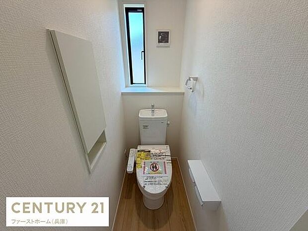 窓付きで明るさが確保されたトイレです。壁面収納がありすっきりとした空間となっています。換気にも配慮されたレイアウトが特徴です。シンプルなデザインで清潔感があります。使い勝手にも配慮された仕様です。