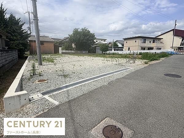 広々とした現地土地写真です。道路に面しており車の出入りもしやすい立地です。周辺には住宅が建ち並び落ち着いた住環境が感じられます。整地されており建築の計画がしやすい土地です。