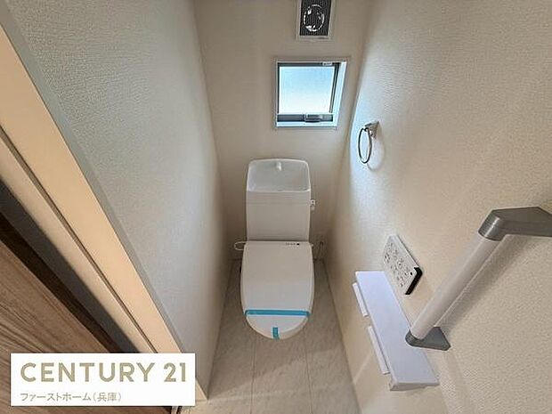コンパクトな空間に設けられたトイレです。窓付きで換気がしやすい環境になっています。清潔感のある内装が特徴です。手すりやペーパーホルダーも配置されています。