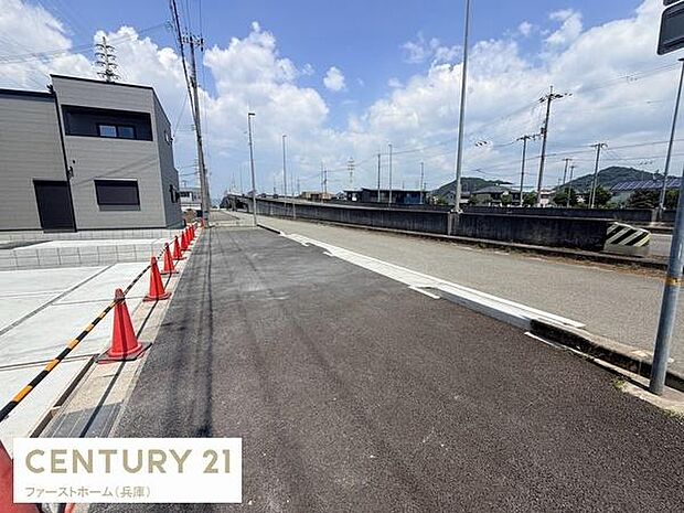 現地写真からは前面道路が広々としており車の出し入れがしやすい印象です。舗装された道路がしっかり整備されています。周辺には電柱やフェンスもあり落ち着いた街並みです。青空の下で明るい雰囲気が伝わります。