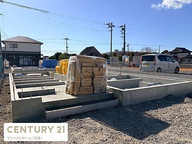 開放的な空の下工事が進む新築住宅の基礎部分が印象的です。資材が整然と置かれており施工の進捗状況がわかります。周囲には建物や車も見え生活環境のイメージもしやすい現場です。