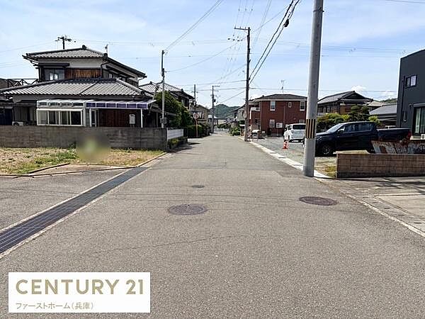 幅の広い前面道路が印象的な現地写真です。周囲には住宅が立ち並び落ち着いた住宅地の雰囲気が広がっています。道路はアスファルト舗装されていて車の通行にも便利です。