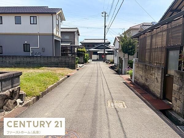 現地前面道路がしっかり整備されており周囲には住宅が建ち並んでいます。周辺には塀や植栽も見られ落ち着いた街並みが広がっています。電柱や電線も整然と配置され交通の視界が確保されています。