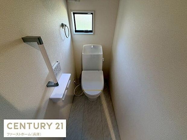 シンプルで落ち着いた内装のトイレです。小窓から自然光が差し込み明るい空間となっています。洗浄機能付きトイレで使いやすさにも配慮されています。清潔感のある床材も特徴です。