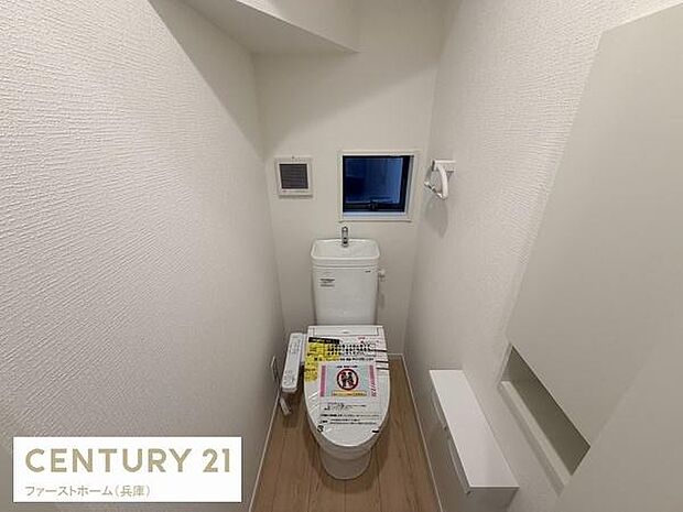 シンプルで清潔感のあるトイレ空間です。窓があり換気がしやすい設計となっています。タンク上部に手洗い場が備わっています。温水洗浄便座も設置されています。白を基調とした内装が特徴的です。